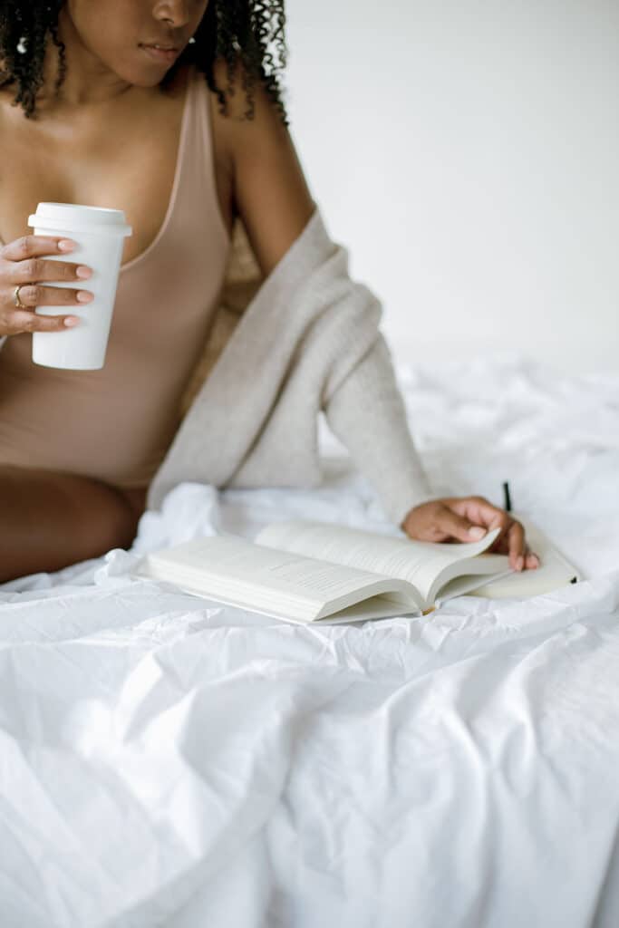 A focused individual sits comfortably with a self-improvement book, pen in hand, and a reusable coffee cup, embodying the essence of personal growth. She is discovering the Best Self-Improvement Books of All Time