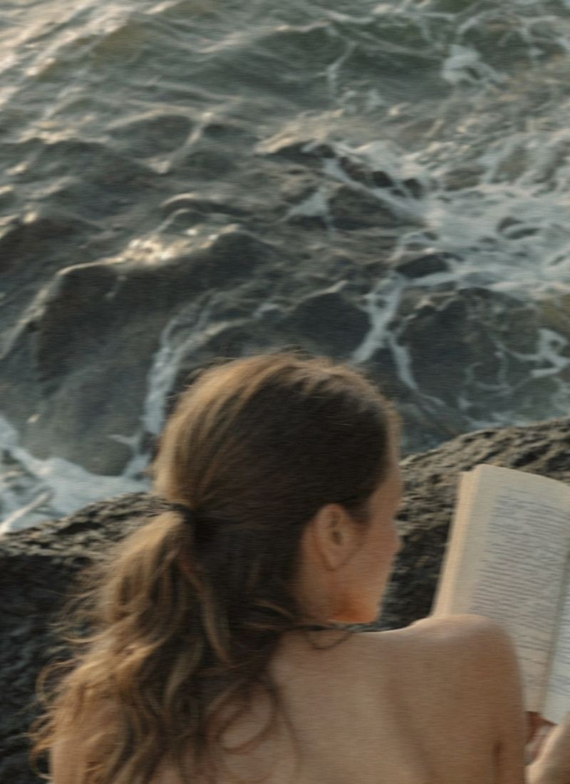 Woman sitting near the water and reading a story