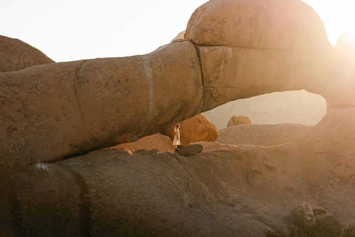 Canadese Model Leigh Dickson stands beneath the natural rock arch in Spitzkoppe, also known as the 'Matterhorn of Africa,' bathed in the warm glow of the setting sun
