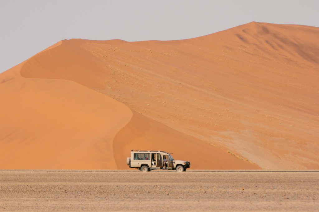 A solitary vehicle travels along the base of the towering orange dunes of Sossusvlei, a striking example of the adventures that await in what to visit in Namibia