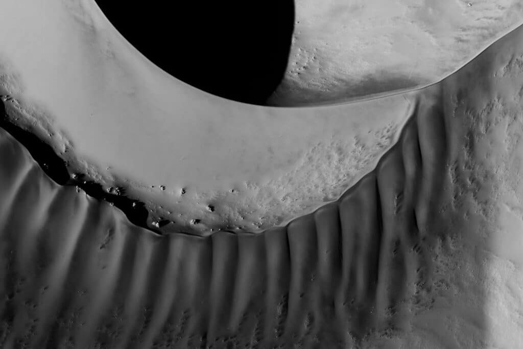 An abstract aerial view of Sossusvlei's dunes in black and white, highlighting the dramatic interplay of light and shadows, a natural marvel to witness when deciding what to visit in Namibia