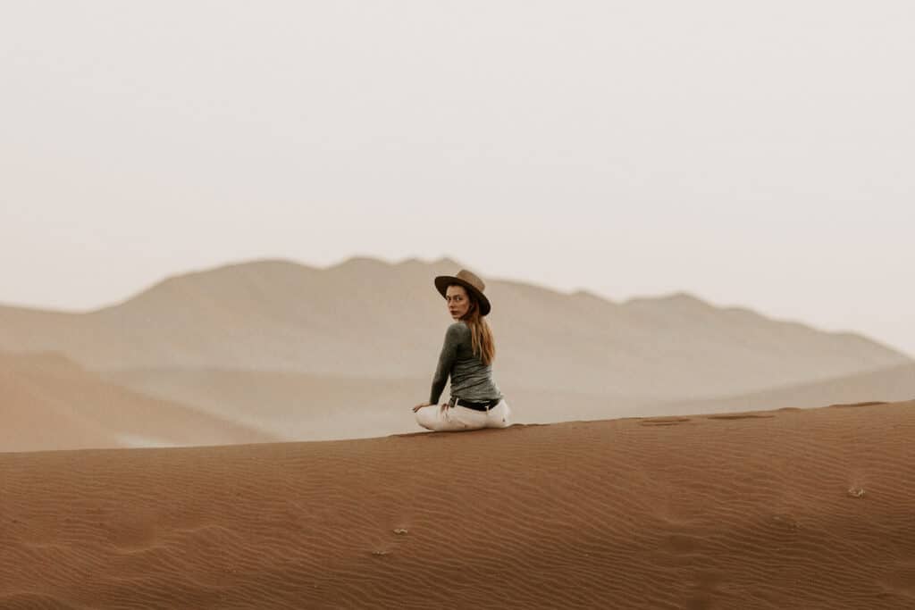 Model Leigh Dickson seated serenely atop a Sossusvlei dune, embodying the tranquil solitude of Namibia's vast desert landscape.