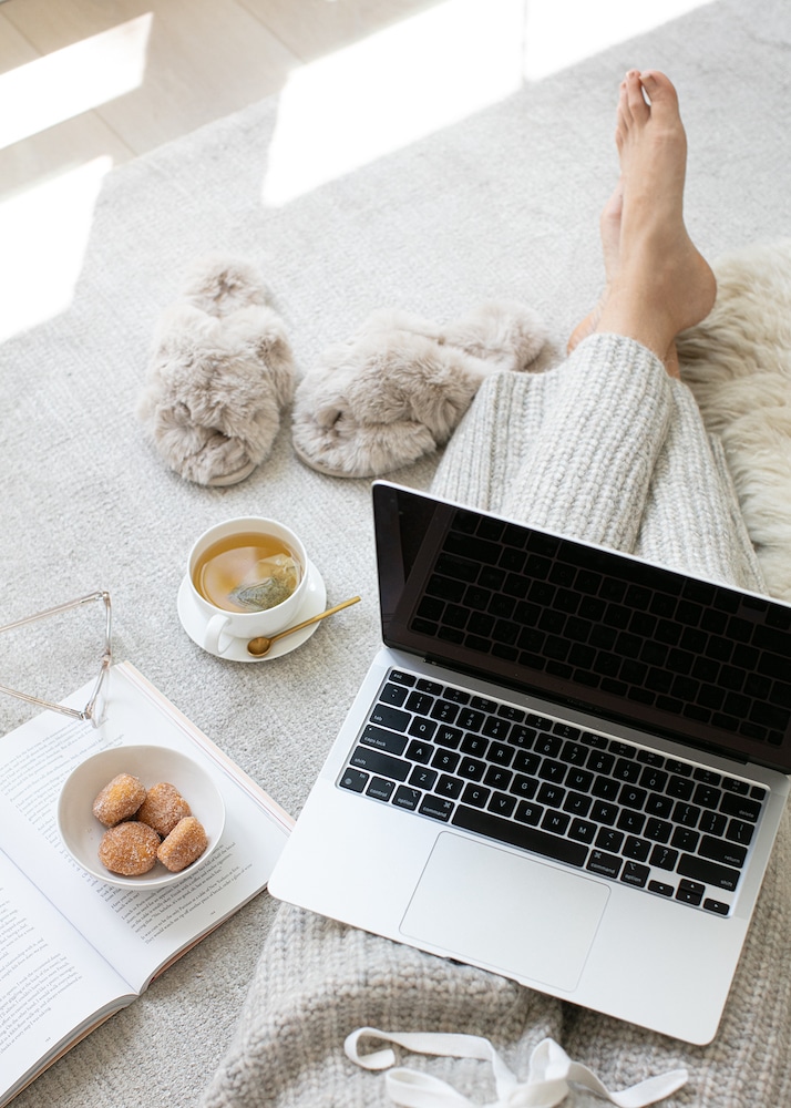 Cozy indoor setting with a laptop, an open book, fluffy slippers, and a cup of tea suggests a peaceful reading environment for Books about Confidence