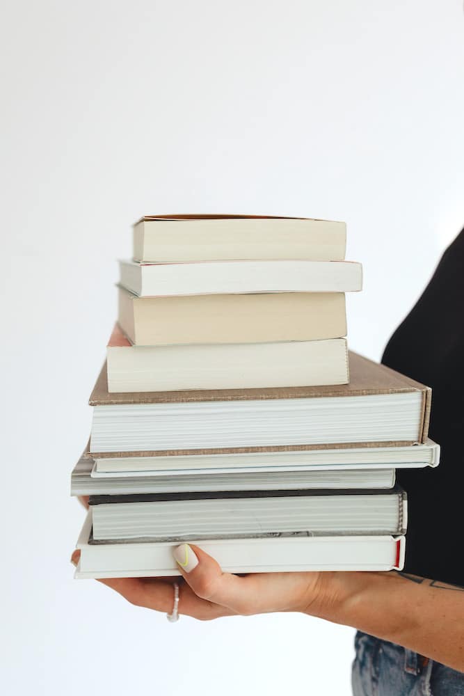 A person holding a stack of hardcover books in preparation to immerse in reading books on self-confidence.