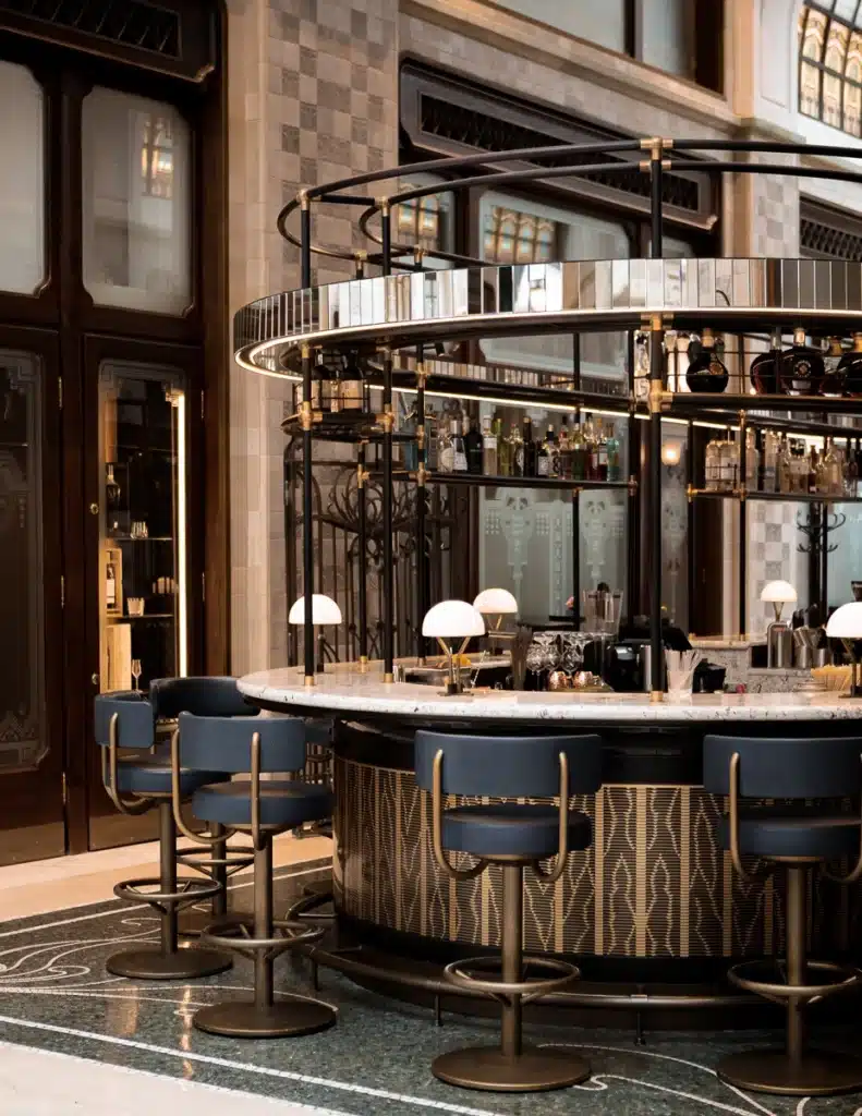 Elegant circular bar with art deco elements and plush blue bar stools set on a marble floor inside the Gresham Palace.