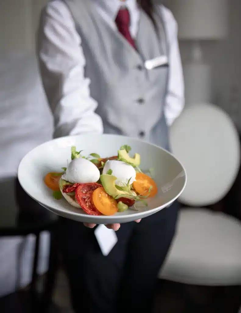 Waitstaff of the Four Seasons Budapest in a crisp uniform presenting a gourmet dish of poached egg and tomato salad