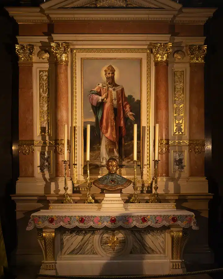 An ornate altar at St Stephen's Basilica featuring a central painting of St. Stephen, with golden candlesticks and a bust below.