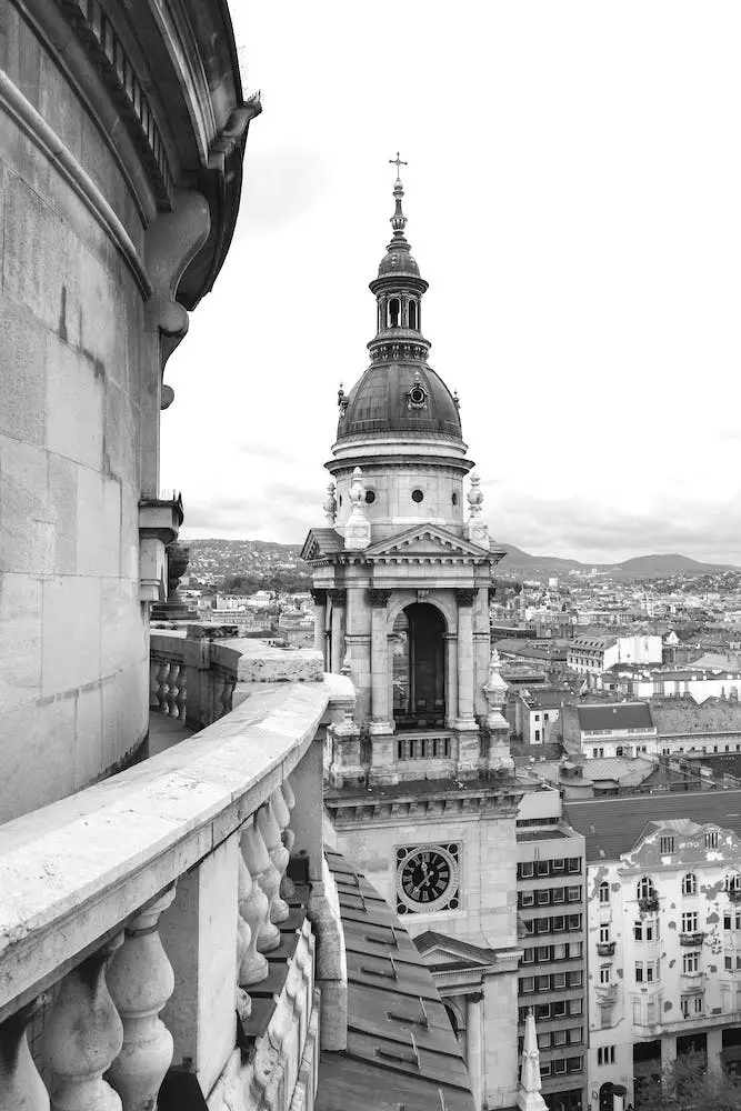 Black and white photo of St Stephen's Basilica's tower in Budapest, with a view of the cityscape and hills in the background.