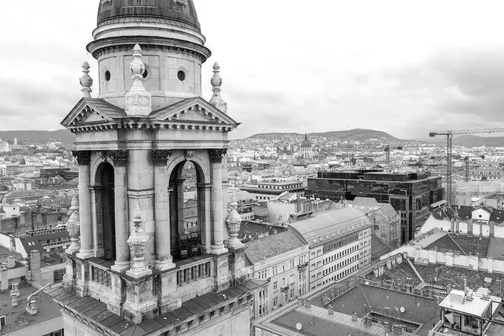 Black and white photograph showcasing a close-up view of St Stephen's Basilica's tower against the sprawling Budapest cityscape.