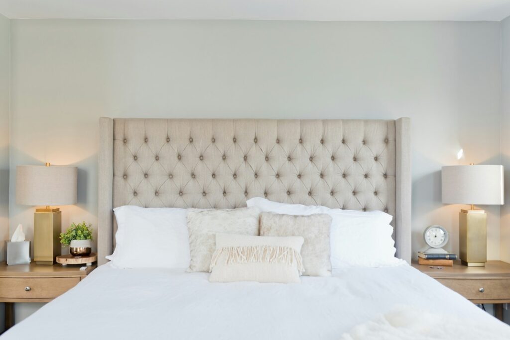 A well-appointed bedroom featuring a tufted headboard, matching bedside tables with elegant lamps, and a soft, textured pillow arrangement.