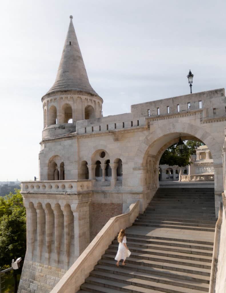 Woman in white dress walking up the stone staircase of Fisherman's Bastion with a turret in the background.