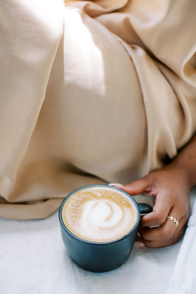 A person cozily wrapped in a silk robe holds a ceramic mug of frothy coffee, symbolizing a relaxed healthy coffee alternatives morning routine.