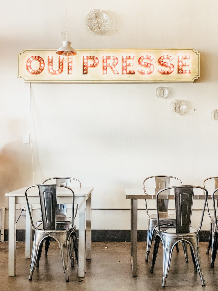A quaint coffee shop interior with a vintage 'OUIPRESSE' neon sign, metal bistro chairs, and white tables, inviting a casual and chic atmosphere offering Healthy Coffee Alternatives