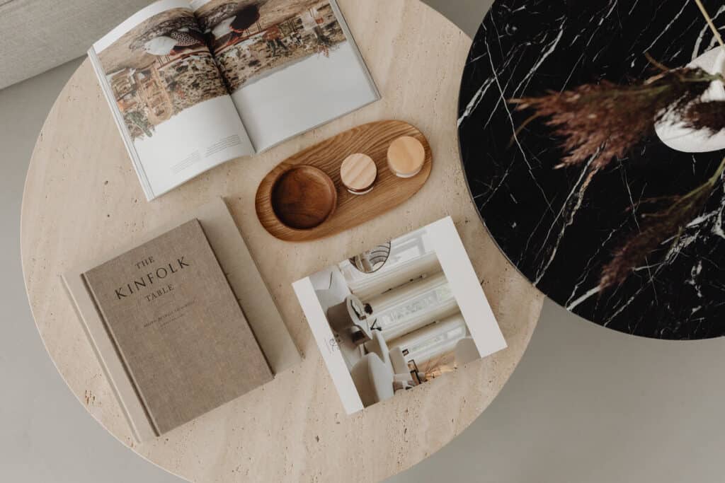 Luxury coffee table books with captivating imagery alongside a chic wooden serving tray on a textured cream-colored table, reflecting upscale interior design.
