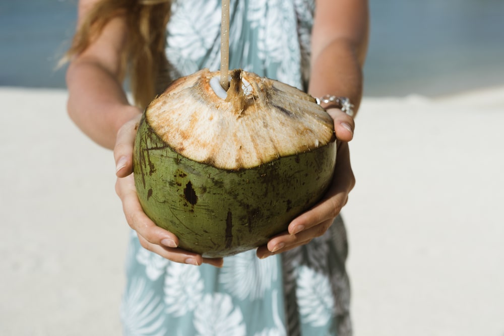 Close-up of a person holding a fresh coconut with a straw on a sandy beach, epitomizing the tropical experience at Île aux Cerfs, a private Island in Mauritius.