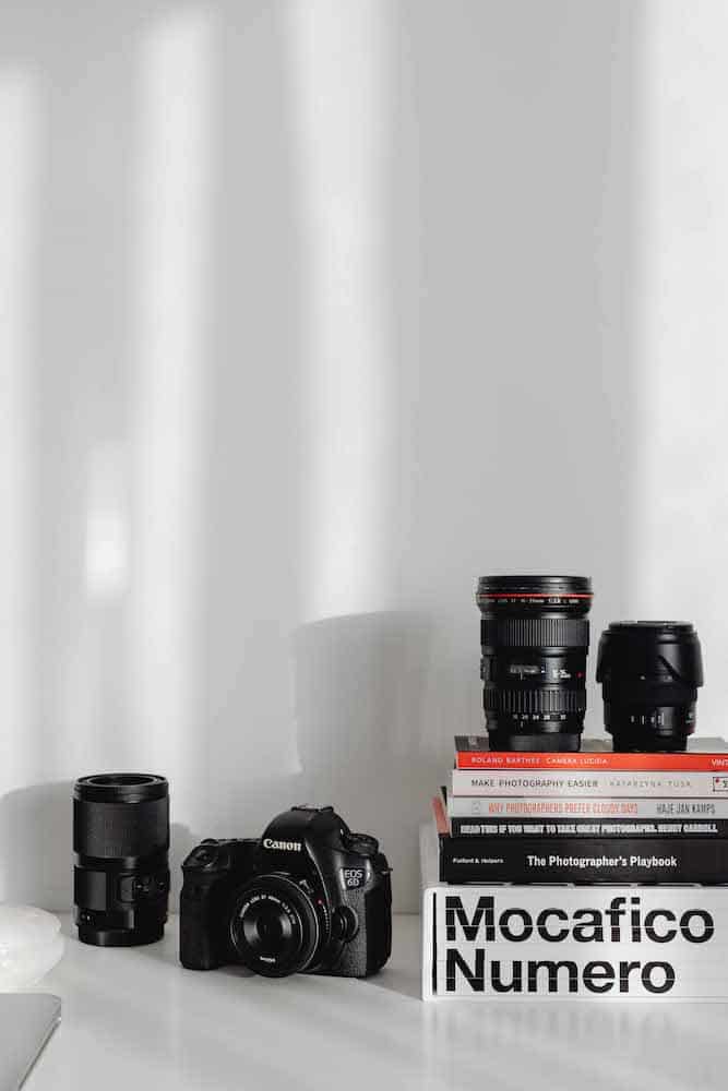 A professional Canon DSLR camera flanked by an array of lenses, set against a backdrop of photography books, creating a curated scene of a photographer's creative space.