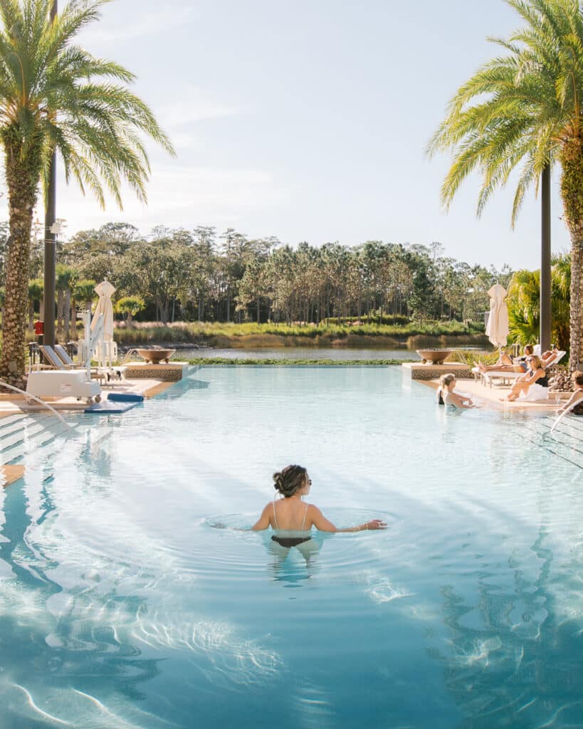 Guest relaxing in the infinity pool at Four Seasons Orlando Disney with view of palm trees and natural scenery.