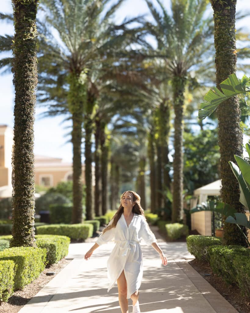 The Blisshunter in a white dress walking blissfully along the palm-lined pathway at Four Seasons Orlando Disney.