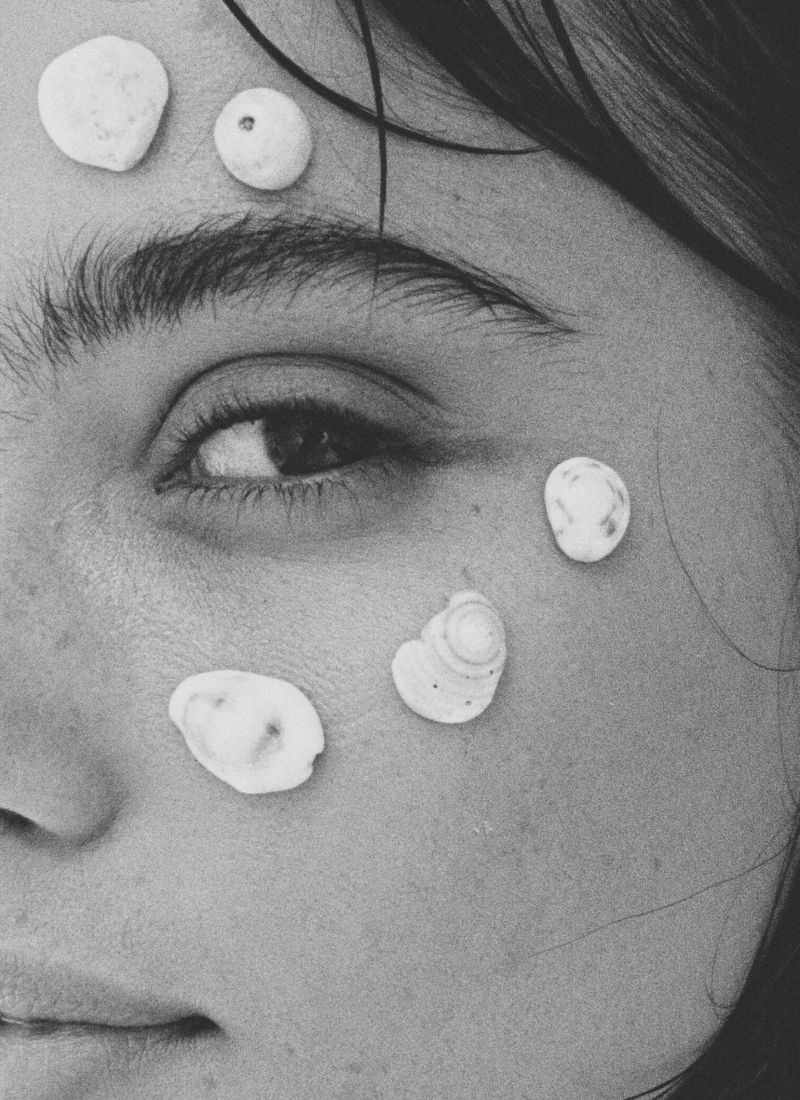 Close-up black-and-white portrait of a woman's face adorned with small seashells, evoking natural beauty and feminine softness
