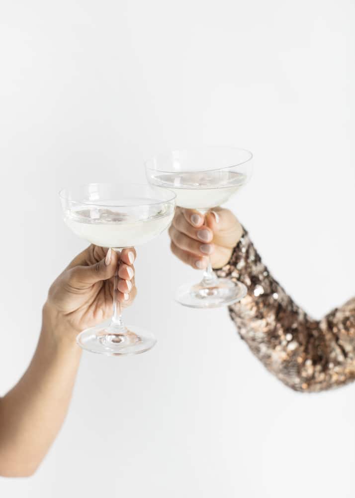 Two hands clinking champagne glasses in a toast for finding the best books about feminine energy.