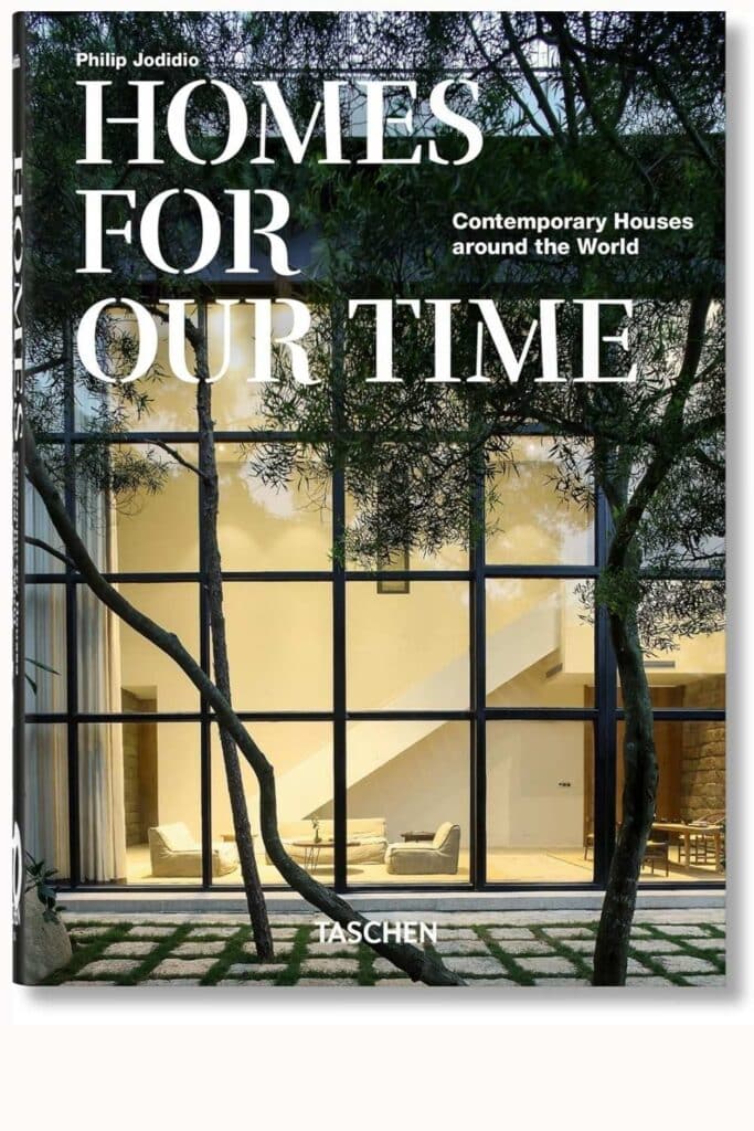 Cover of the coffee table book 'HOMES FOR OUR TIME' by Philip Jodidio, featuring a modern house behind a geometric iron gate and green foliage.