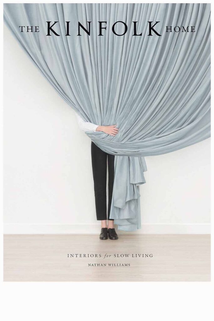 Luxury books: 'The Kinfolk Home' cover with a minimalist aesthetic featuring draped blue fabric and a person standing behind it, symbolizing interiors for slow living.