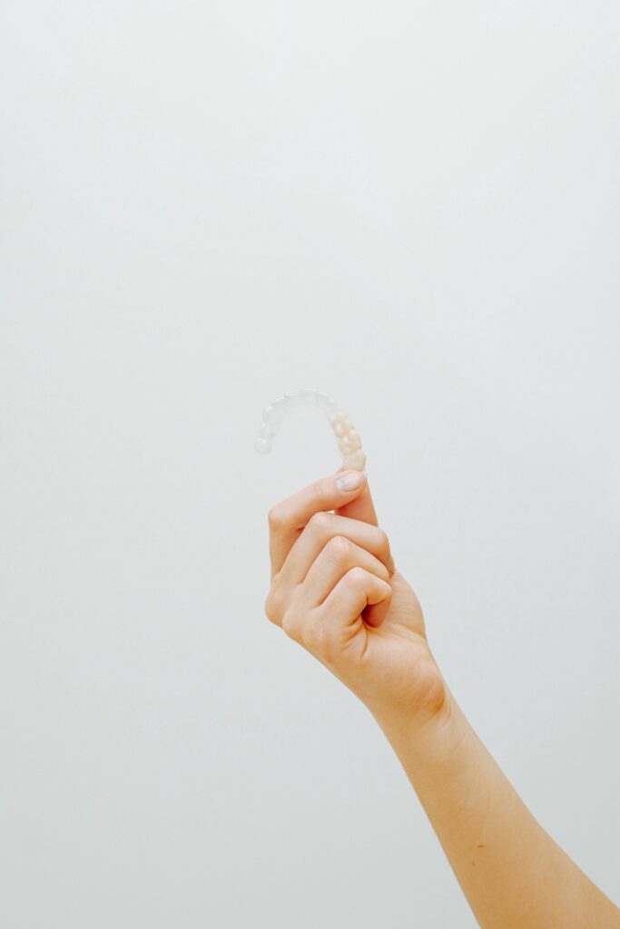 Is Invisalign Worth It for Adults? My Comprehensive Review - A hand holding up a clear Invisalign aligner against a plain white background, highlighting the transparency and design of the orthodontic device.