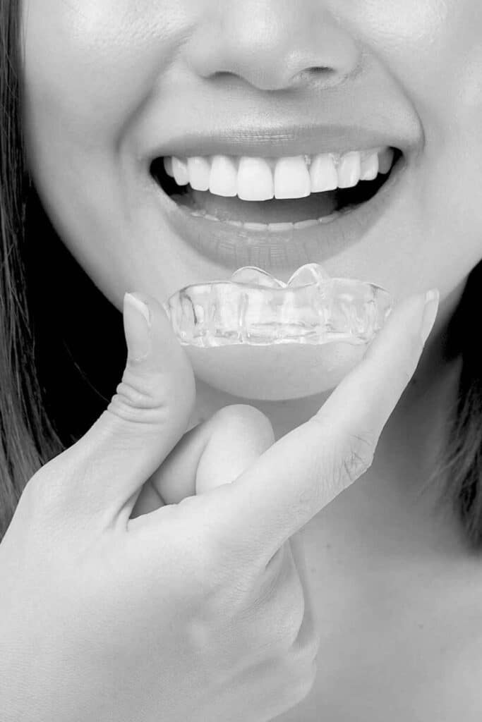 Is Invisalign worth it for adults? Close-up of a smiling woman inserting a clear Invisalign aligner, highlighting the ease of use for adults considering orthodontic treatment.