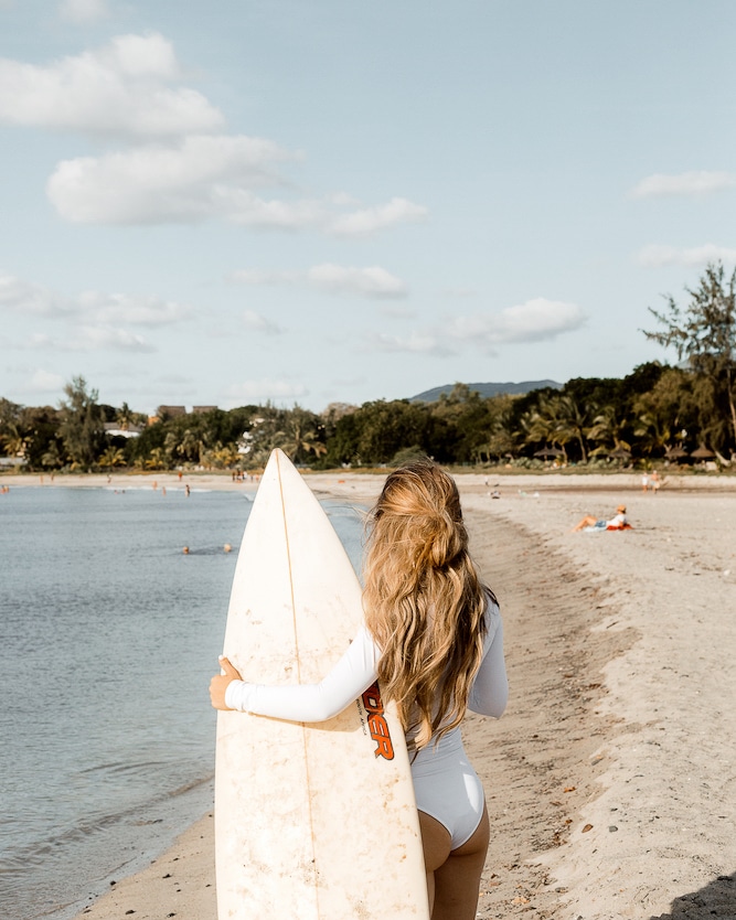 A surfer, The Blisshunter, gazes out at the sea in Mauritius, holding a surfboard and contemplating the island's appeal, perfectly capturing the adventurous spirit that answers 'Is Mauritius worth visiting?'