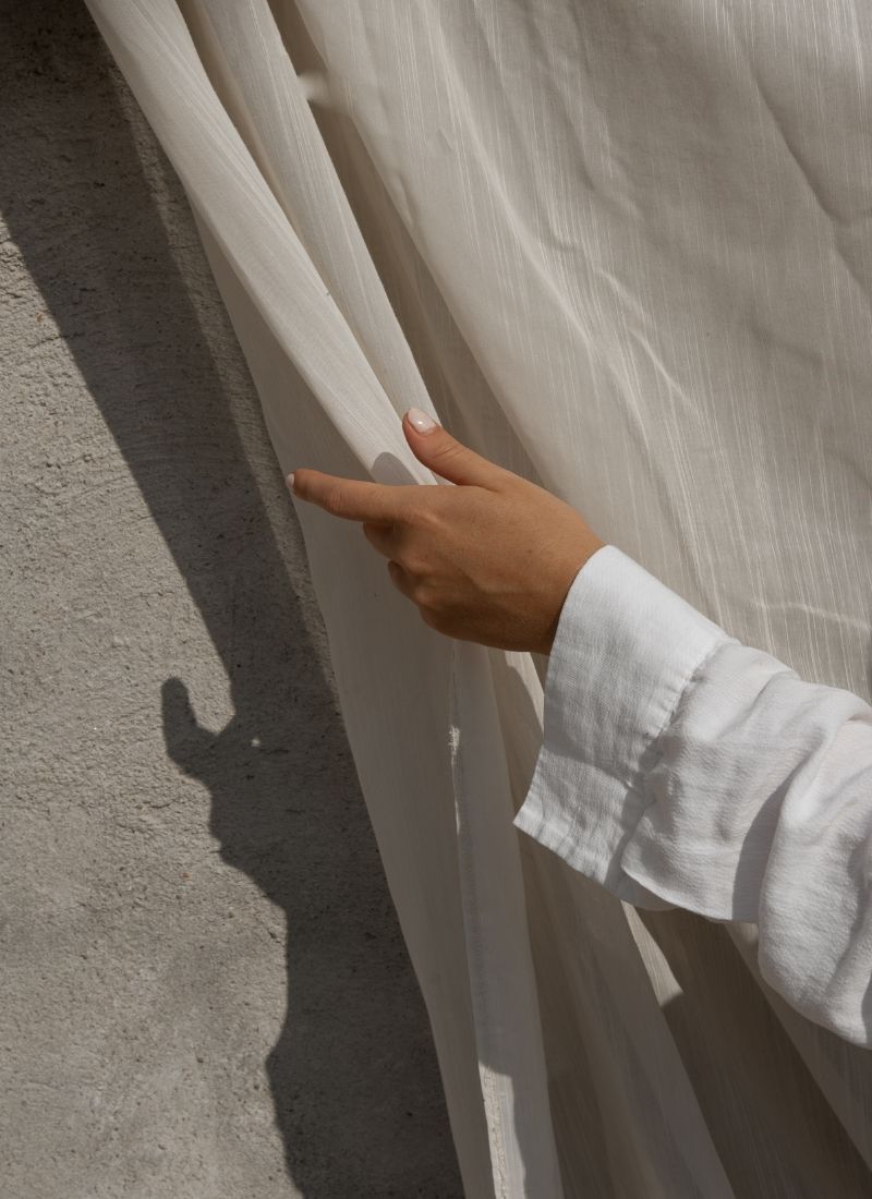 Hand gently parting a light linen curtain in soft natural light