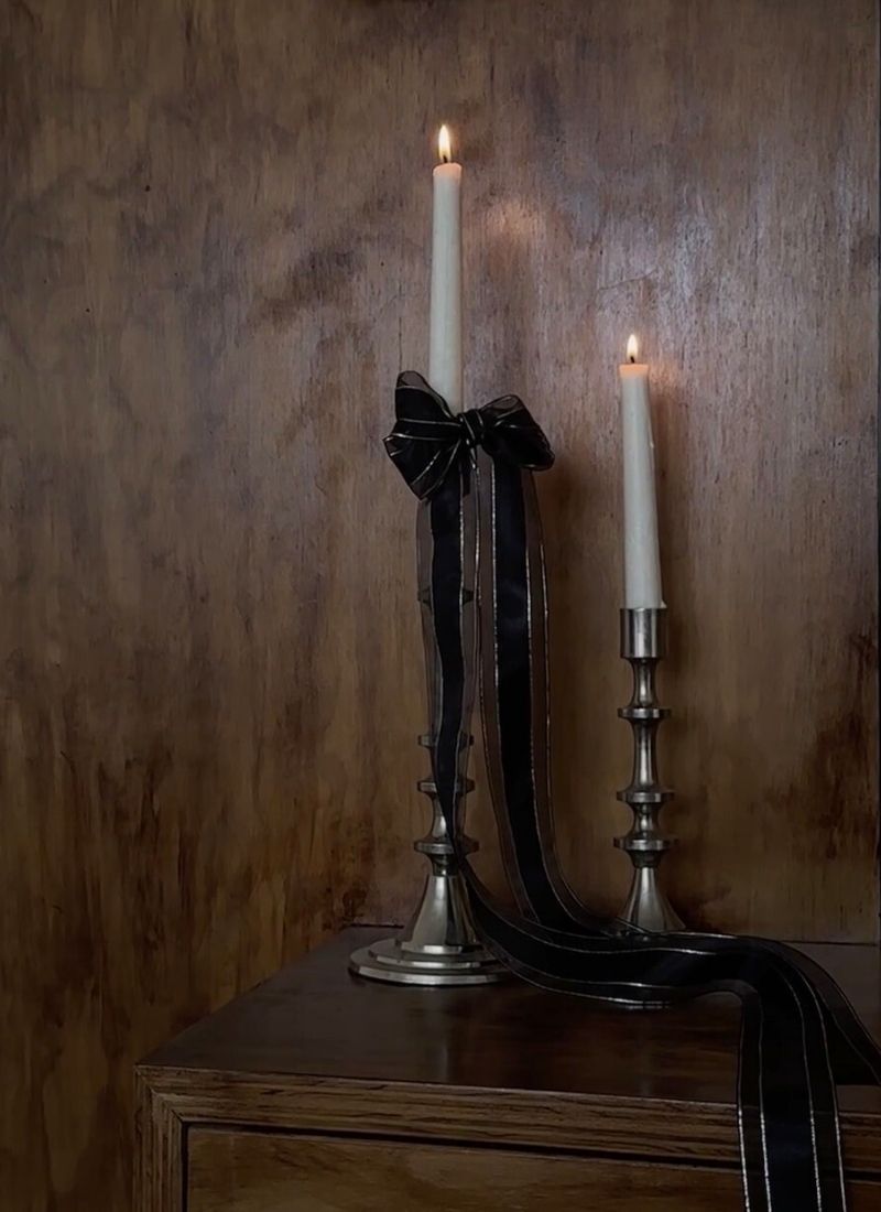 Two lit candles on silver holders with a black ribbon, creating a moody, elegant bedside atmosphere.
