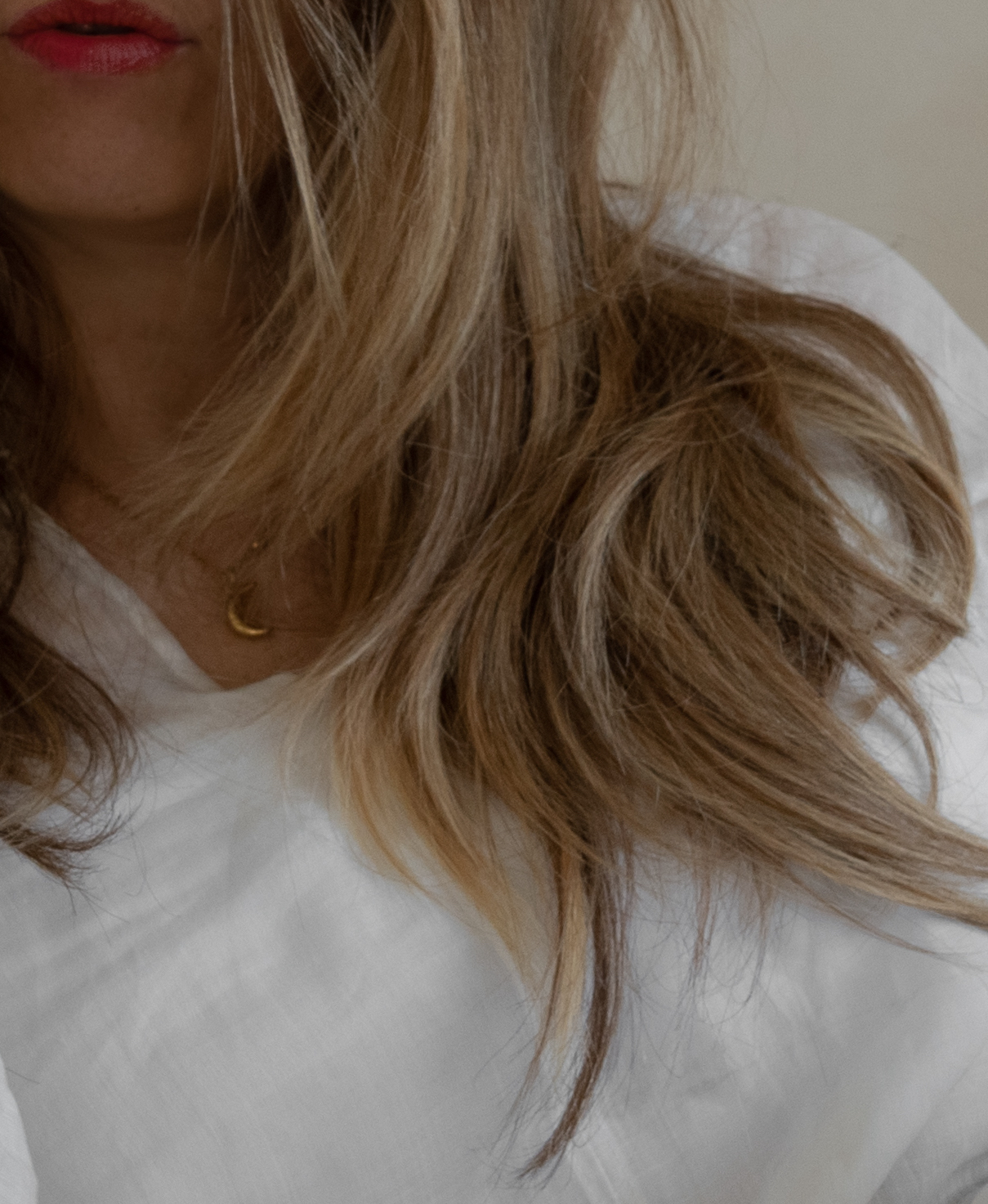 Close-up of a woman in a white linen blouse with tousled hair and a gold moon necklace, symbolizing softness and feminine energy.