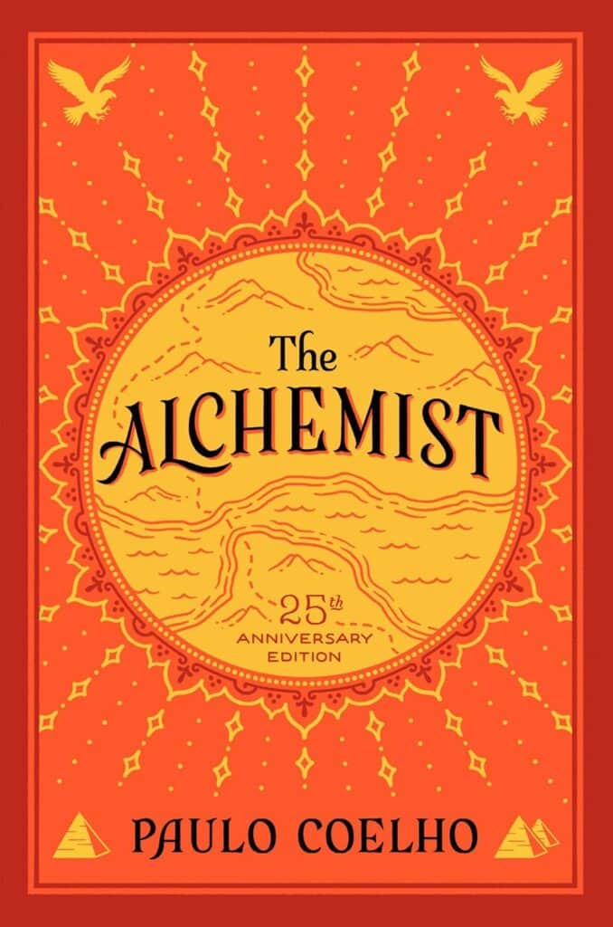 Cover of 'The Alchemist' 25th Anniversary Edition by Paulo Coelho, featuring ornate golden patterns on a rich red background with a central motif of a mountain landscape.