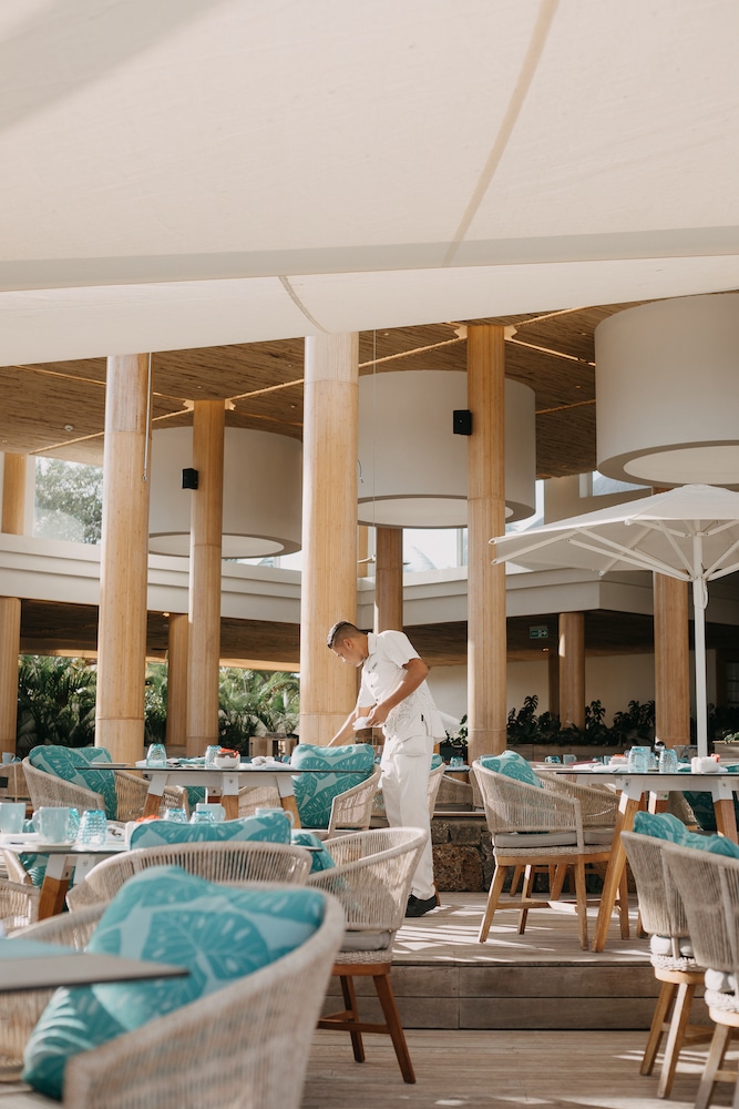 A waiter prepares a table with meticulous care in the sunlit dining area of the Four Seasons at Anahita, one of Mauritius 5 star hotels.