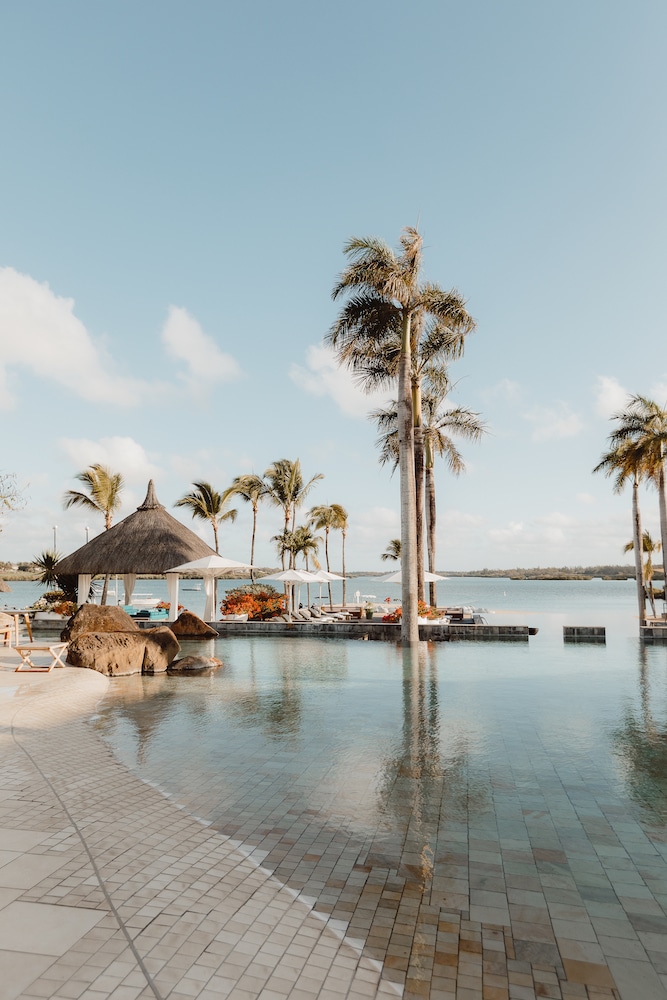 Tranquil infinity pool edged by towering palms and thatched gazebos at the Four Seasons at Anahita, one of the best luxurious Mauritius 5 star hotels.