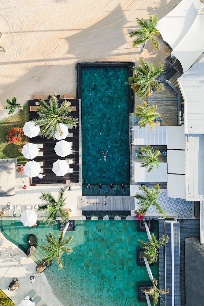 Aerial view of a luxurious pool at a Mauritius 5 star hotel, with a single swimmer enjoying the tranquil waters amidst a layout of sun loungers and tropical palms.