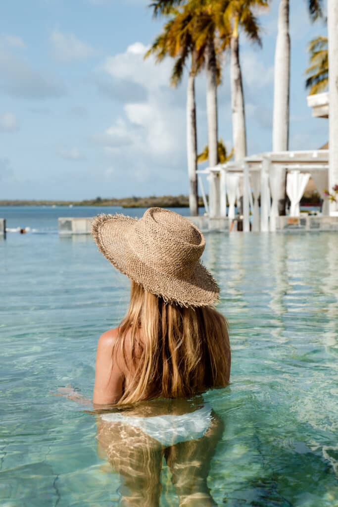 A woman in a straw hat gazes out over the infinity pool at a luxurious  5-star hotel in Mauritius, embodying a sense of peace and relaxation.