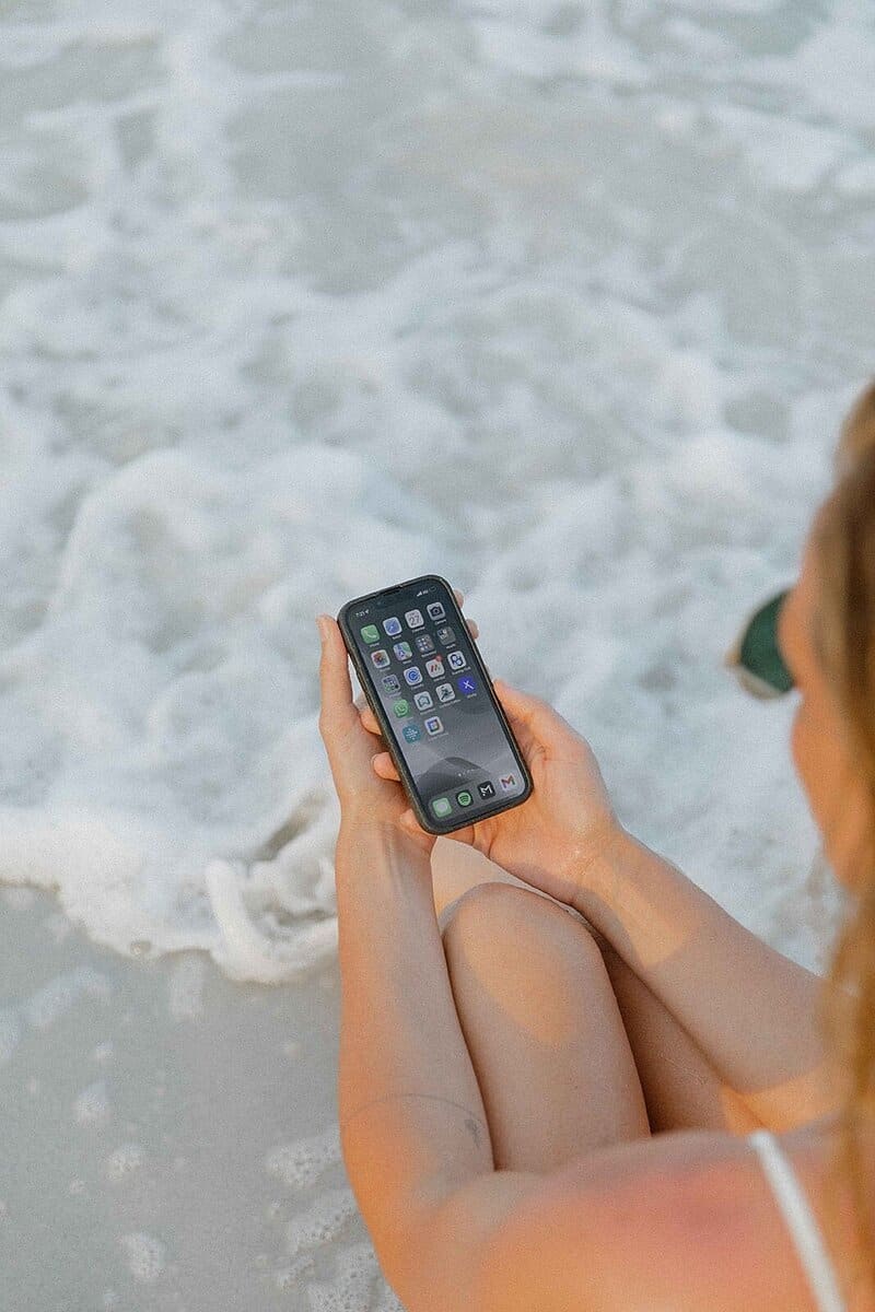 A person sitting on the beach holding a smartphone, contemplating how to delete their Instagram account for a digital detox.