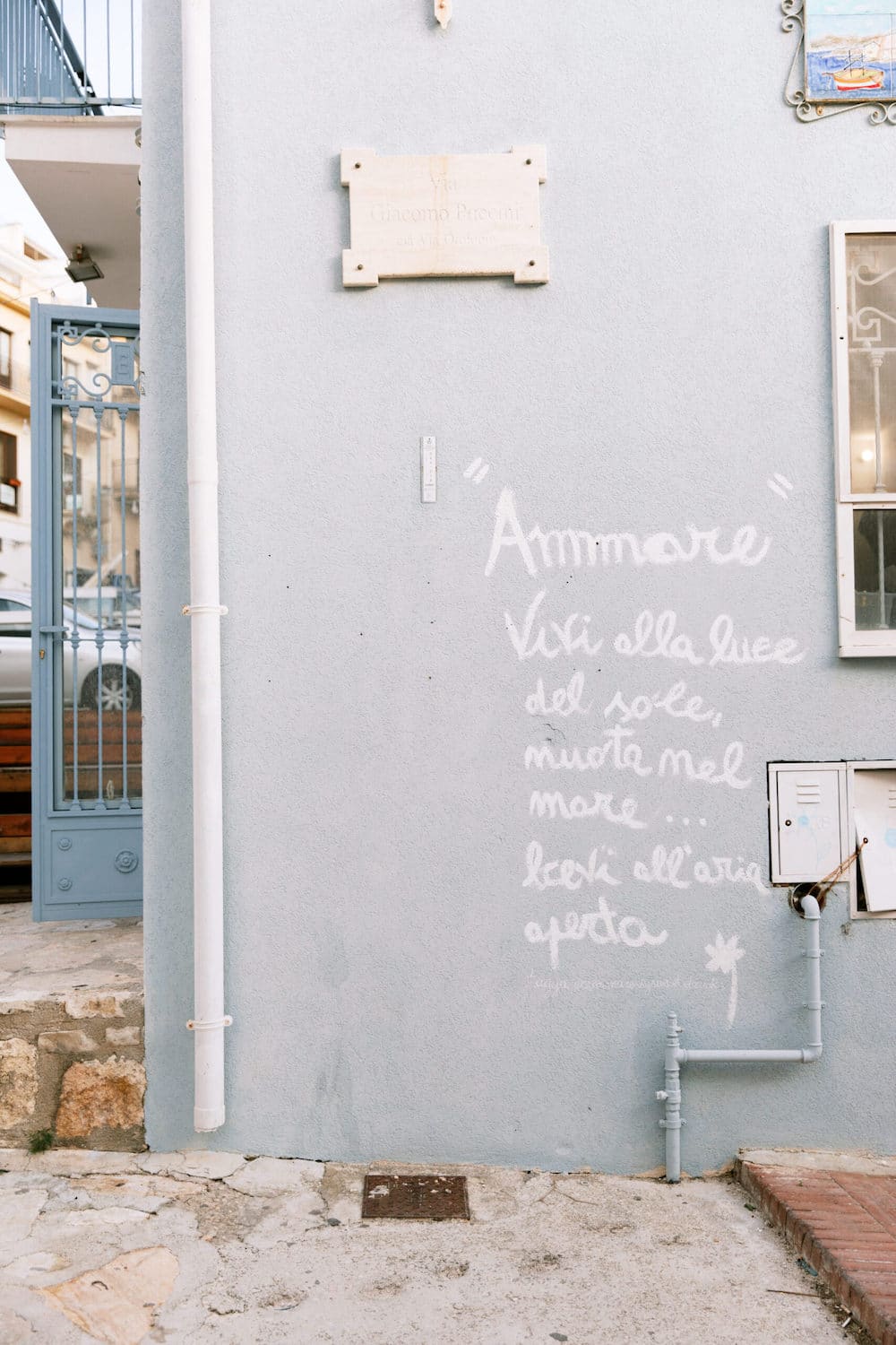 White painted Italian quote on a blue wall expressing love and life's simple joys, symbolizing the essence of short spiritual quotes for healing and strength.