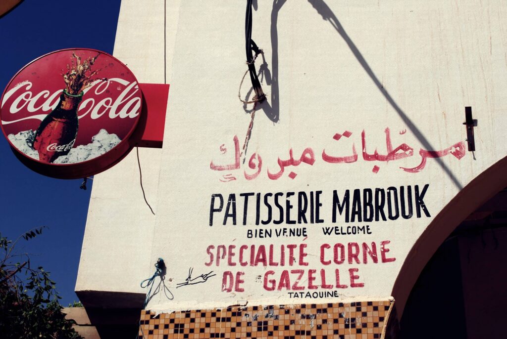 A vintage Coca-Cola sign above Arabic script and French patisserie signage, indicating the cultural fusion of a streetside bakery in Djerba. - your answer to Is Djerba Worth Visiting?